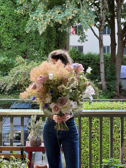Grande seasonal bouquet with 25+ stems of smoke bush, blush roses, lisianthus and cornflowers, so large it hides the person holding it, by Portland florist Kvetka Flower