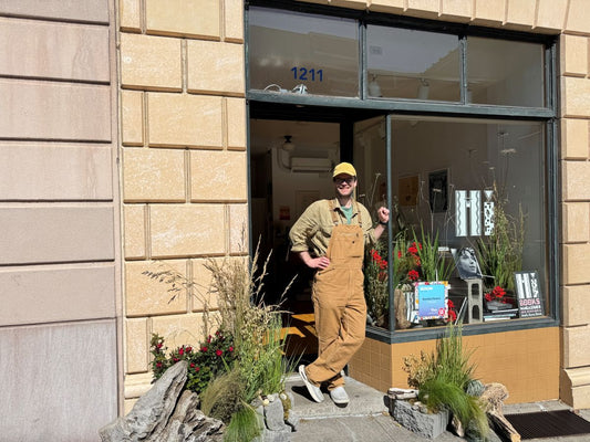 Kvetka Flower owner standing in the doorway of Hi Books bookshop with the completed driftwood floral installation for Bloom Tour Portland 2026
