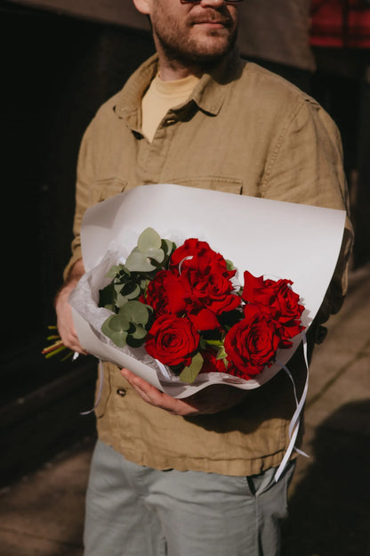 Handcrafted dozen red roses bouquet held in hands for Valentine's Day