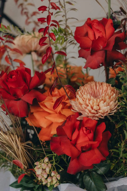 Vibrant red and orange roses with chrysanthemums in seasonal flower basket arrangement