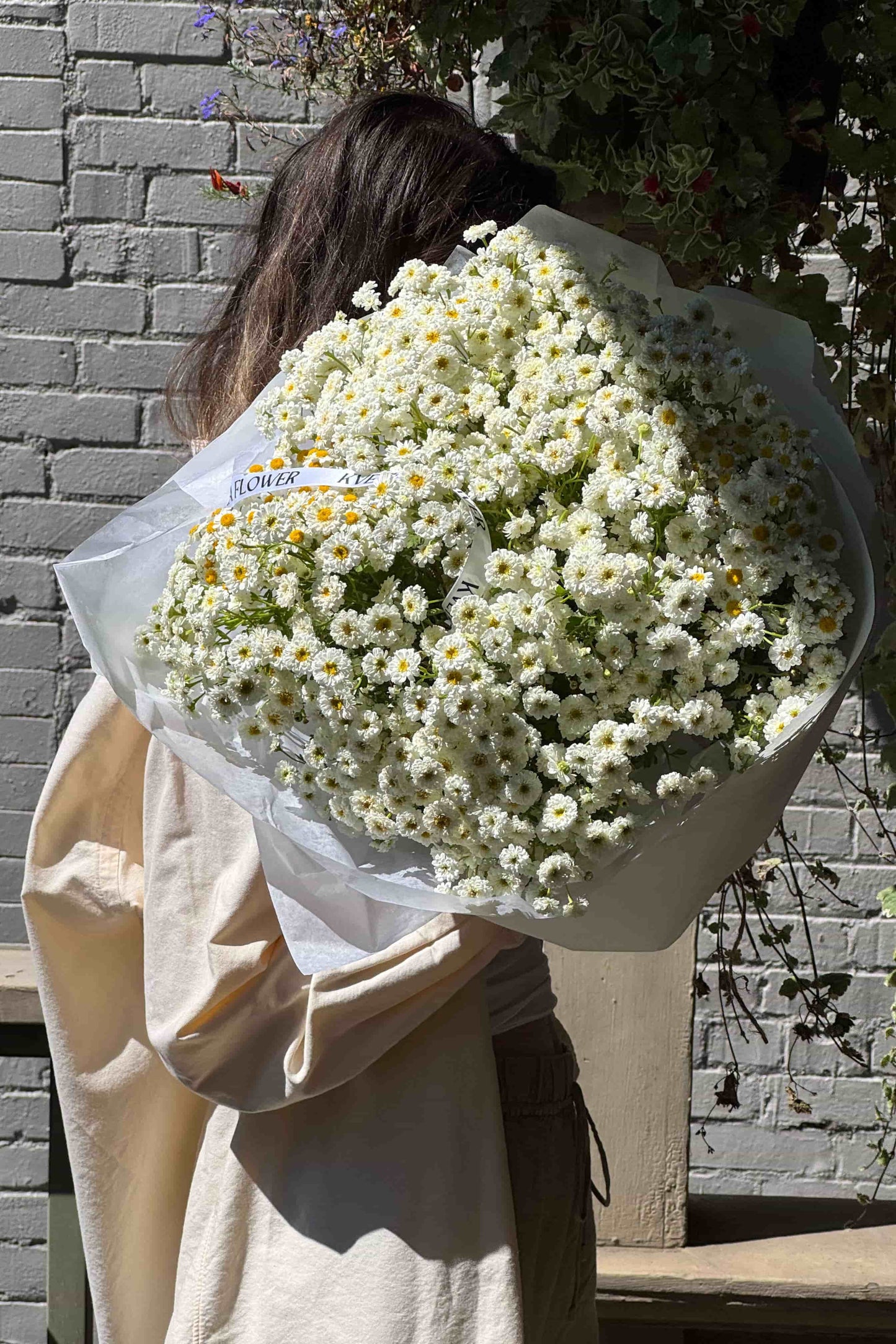 Woman holding a large bouquet of chamomile flowers in Portland sunlight – Kvetka Flower summer blooms