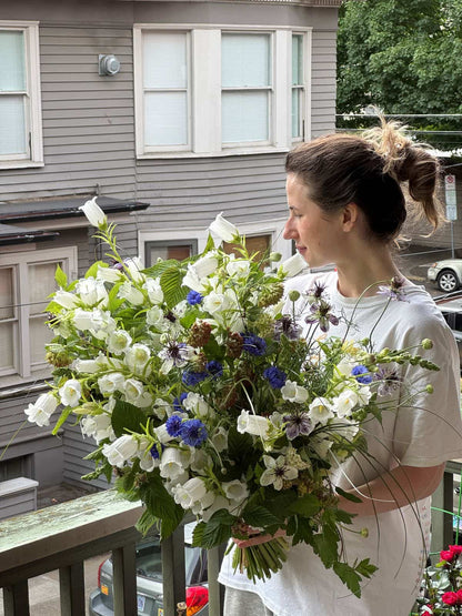 Woman holding an extra large white and blue bouquet with bell-shaped campanula, blue cornflowers and nigella, by Kvetka Flower Portland