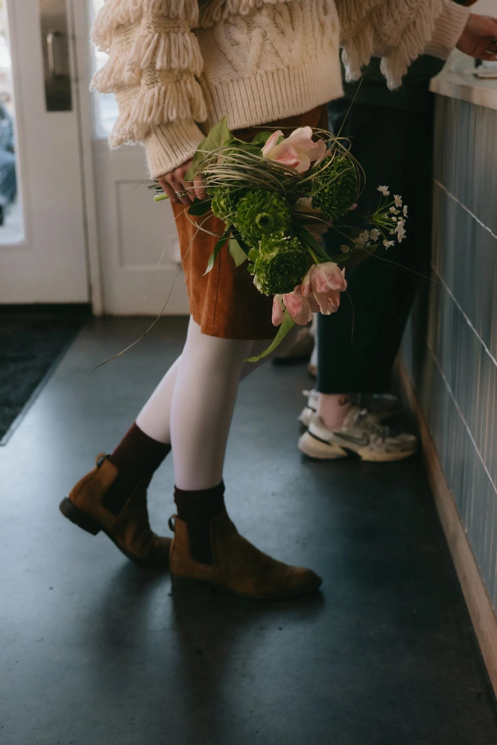 Woman holding green textured bouquet with seasonal blooms in Prince Cafe in Portland, Oregon