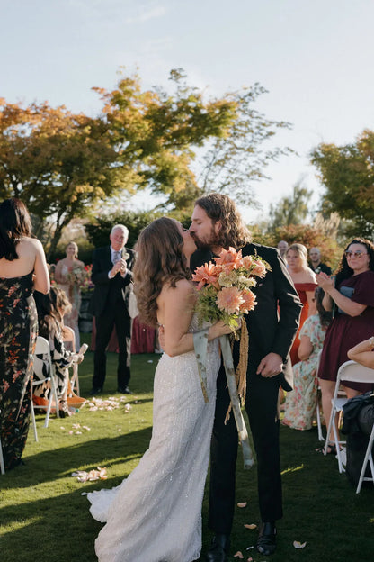 Bride and groom kiss during recessional, bride holding trailing chrysanthemum bridal bouquet by Kvetka Flower