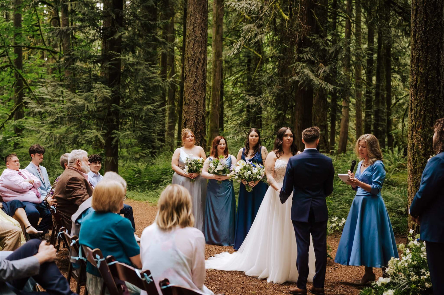 Bride and groom exchange vows surrounded by trees and bridesmaids at Camp Colton – by Kvetka Flower, Portland OR
