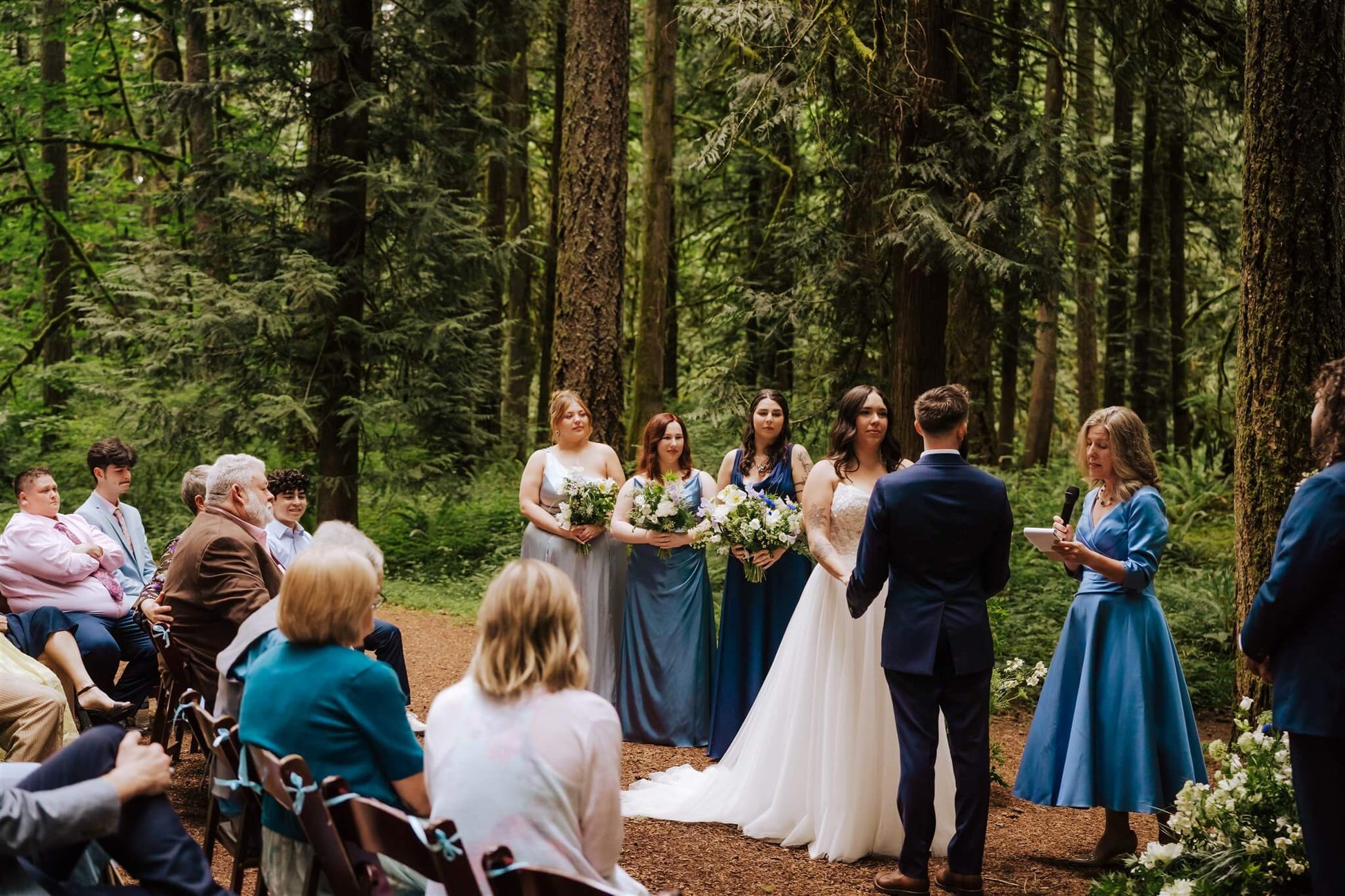 Bride and groom exchange vows surrounded by trees and bridesmaids at Camp Colton – by Kvetka Flower, Portland OR
