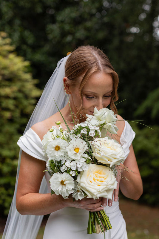 Close-up of bride with whimsical white bridal bouquet featuring garden roses, white cosmos and dianthus by Kvetka Flower