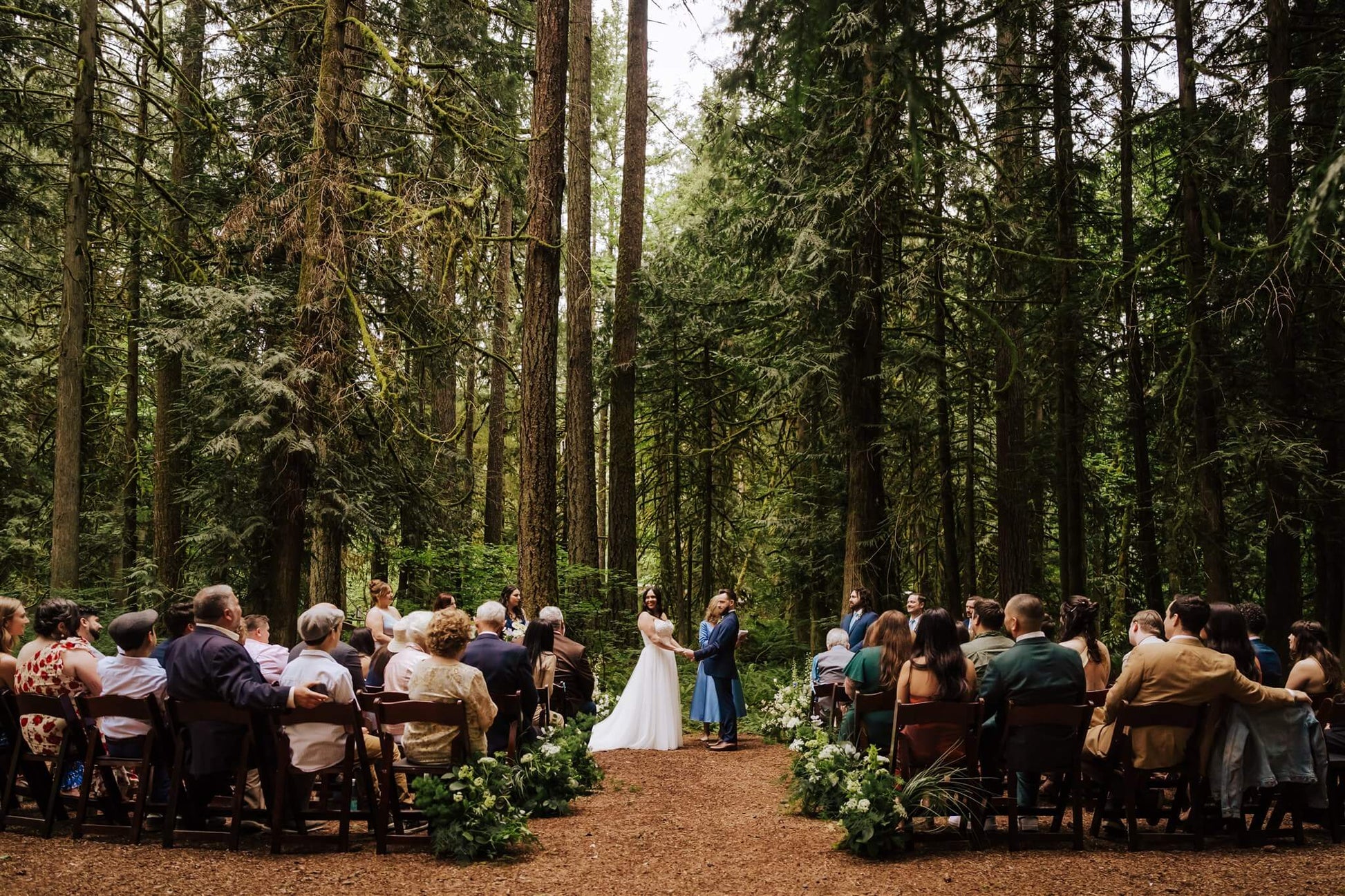Wide shot of the ceremony in the woods at Camp Colton with guests and floral decor – by Kvetka Flower, Portland OR