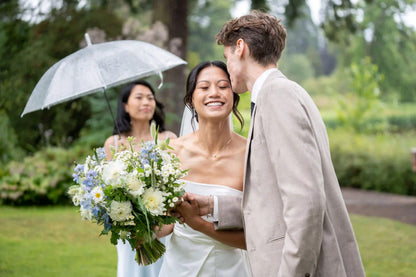 Bride and groom sharing a moment with Kvetka Flower bouquet while bridesmaid holds umbrella in Portland, OR